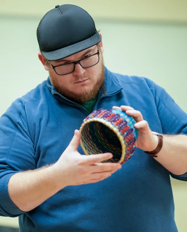 A student holds a colorful Wabanaki woven basket