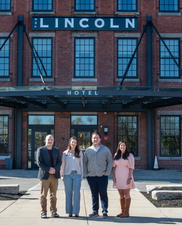 UNE business leaders and a student pose inside The Lincoln Hotel lobby