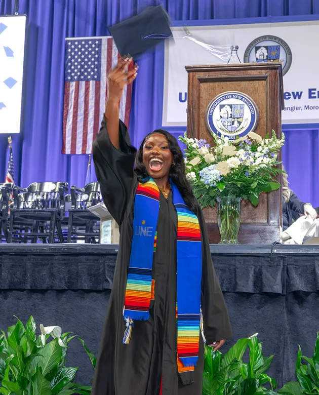 A graduating student in regalia throws their cap in the air