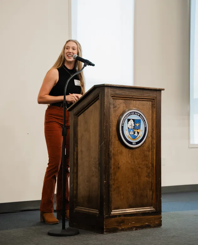 UNE fellowship alum Juliann Lapierre ’24 speaks at the podium