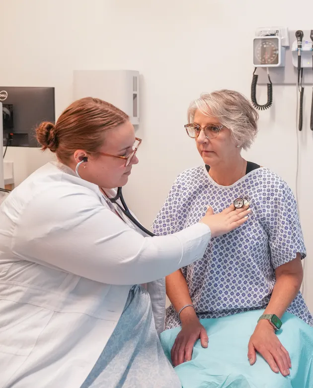 A C O M student listens to a patient's heart with a stethoscope