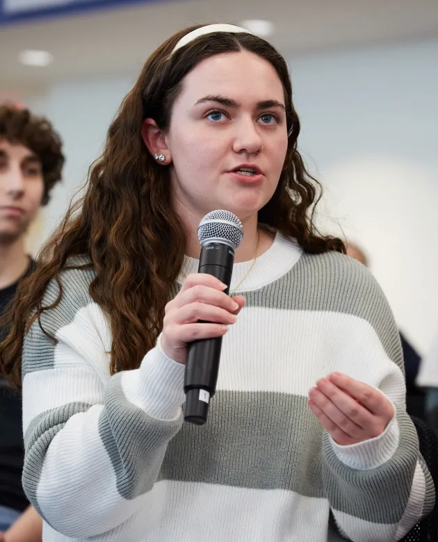 A student holding a microphone asks a question during an event