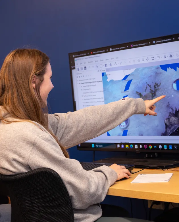 A student points to their 3 D model on a large monitor