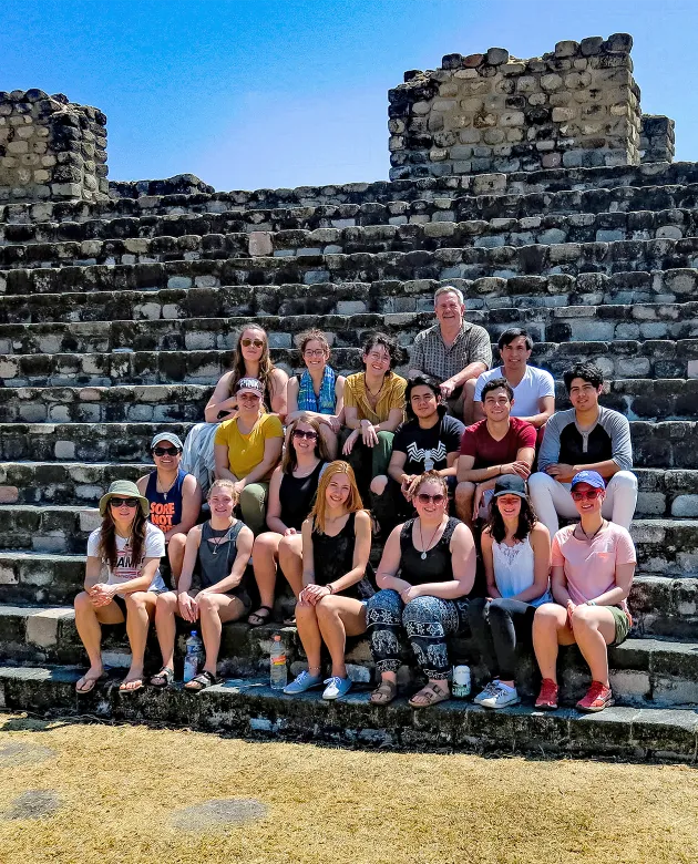 A group of students sit together on stone steps of ruins in Mexico