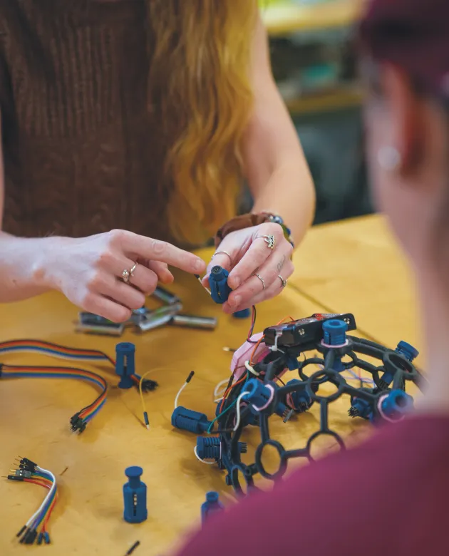 Jessica Howard assembles electronic components and wires into a skull cap on a yellow work table.
