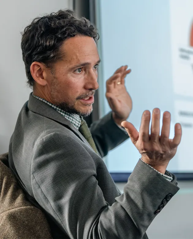Ken Courtney gestures while speaking during presentation with pie charts visible on screen behind him.