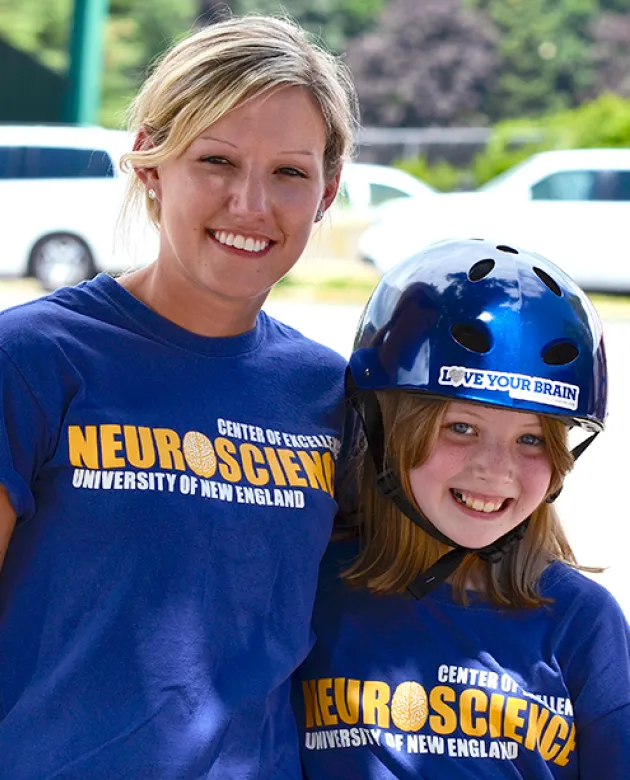 A U N E student stands with a kid wearing a bike helmet for a neuroscience outreach program