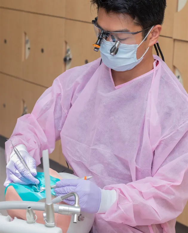 A dental medicince student wearing pink scrubs practicing skills in the Oral Health Center