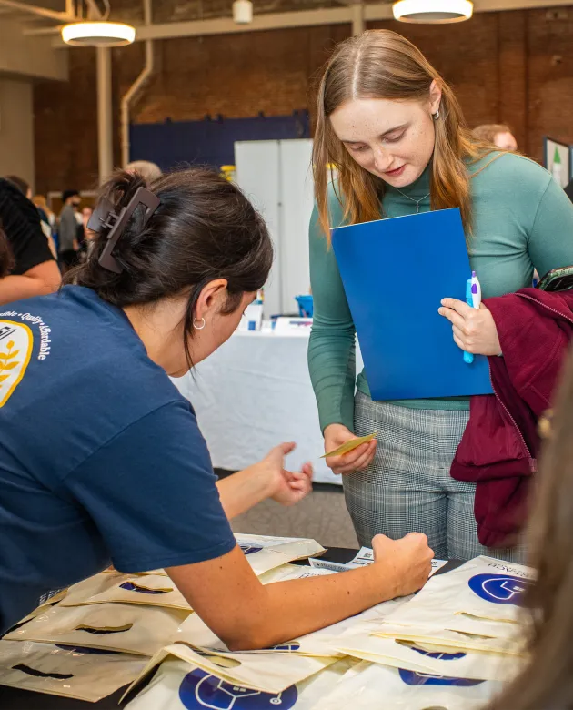 A U N E College of Dental Medicine student holds a folder while getting information from a vendor at a career fair.