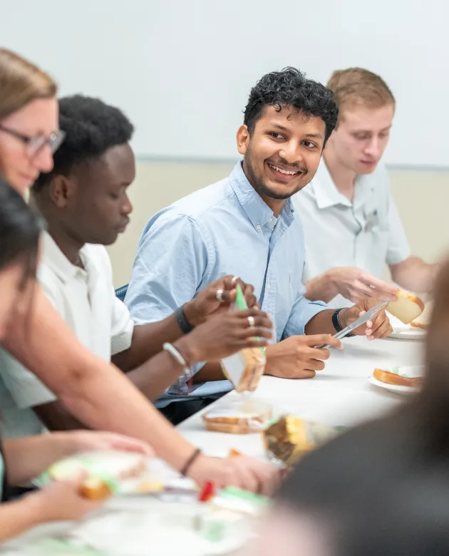 U N E students volunteer together at a long table making peanut butter and jelly sandwiches during a service-learning event.