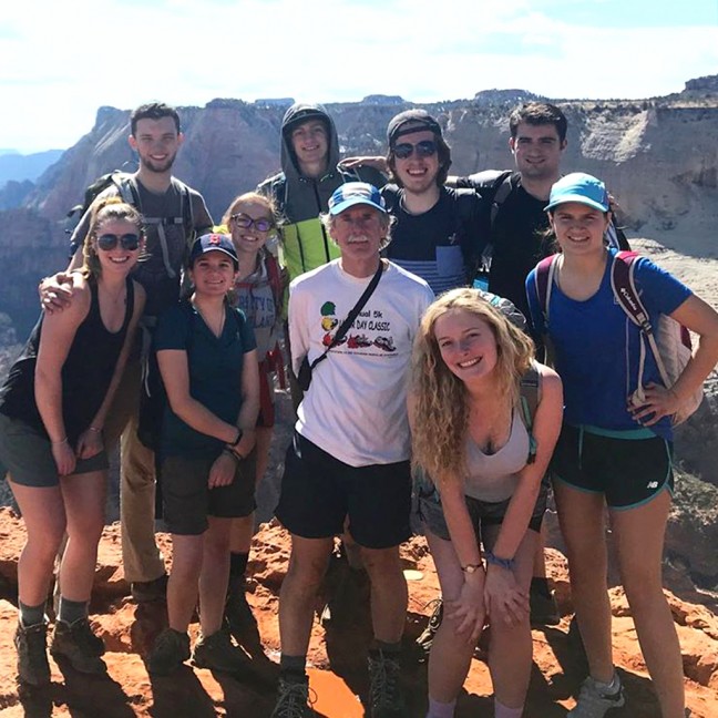 A group of students and a faculty member pose on the top of a mountain after a hike