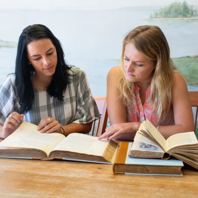 two students study together at a table with multiple books