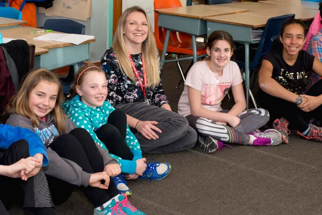 A teacher sits on the floor with her young students