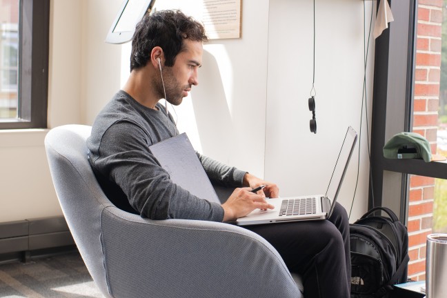 a student sits in an armchair working on a laptop