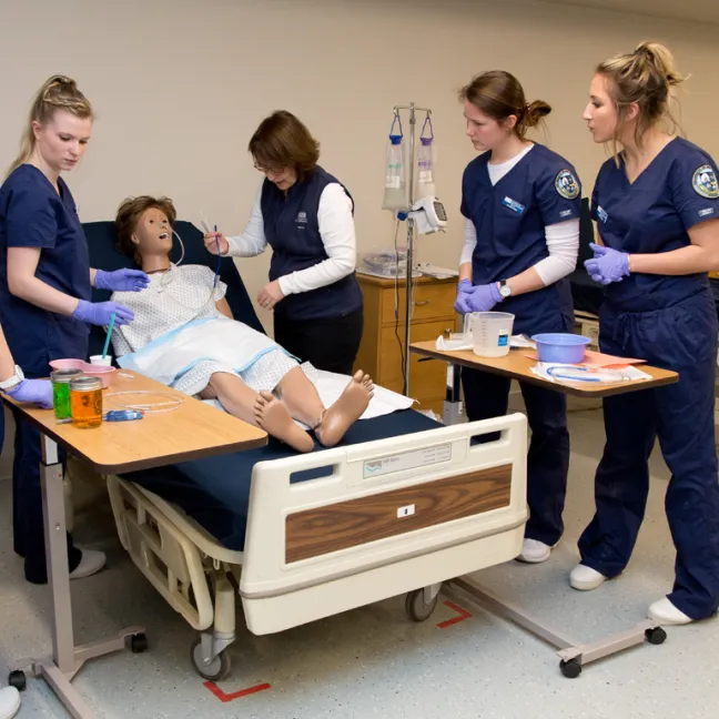 three students and a professor work on a patient simulator