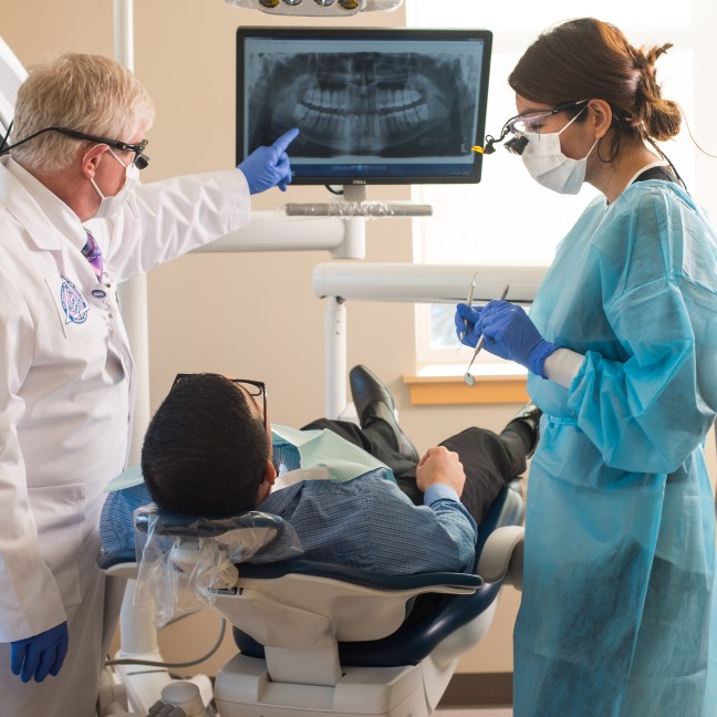 A student and instructor show a patient an x-ray of his teeth in the Oral Health Center