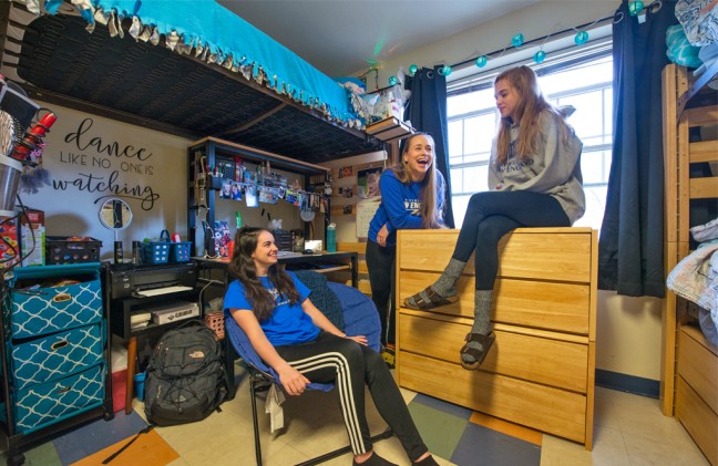 Three students talking and laughing in their dorm room