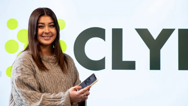 Abbie Anderson poses with a mobile phone. The name of her app, Clyk, is shown behind her.