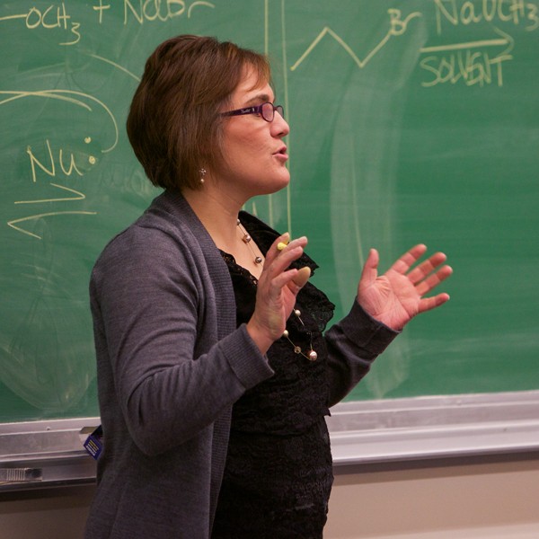 A faculty member stands in front of a chalkboard