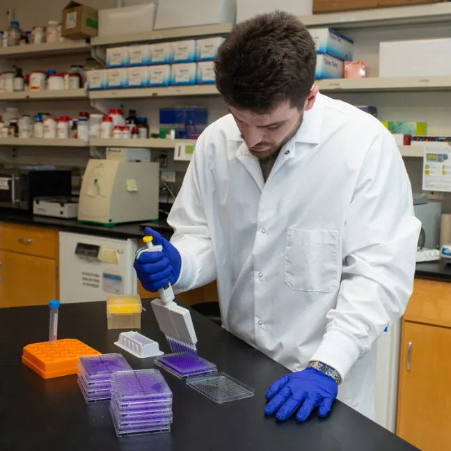 A student in a white coat dispenses liquid into a container