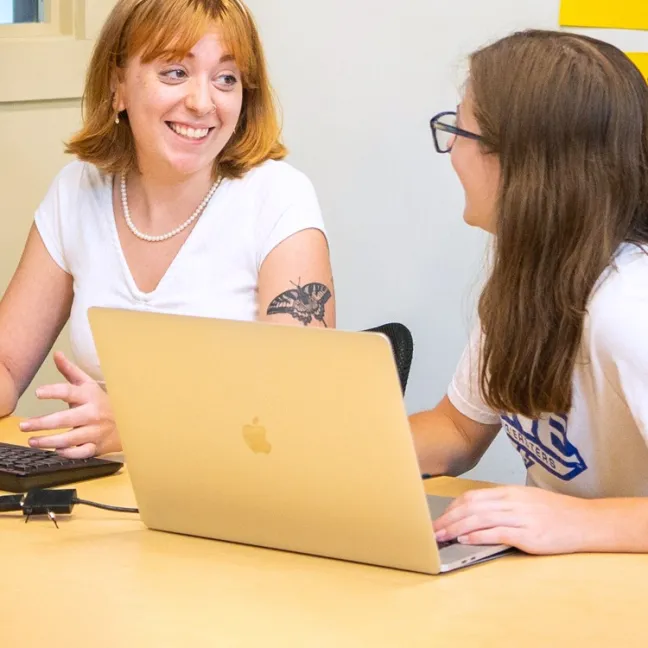 Two computer science students talk in front of a laptop