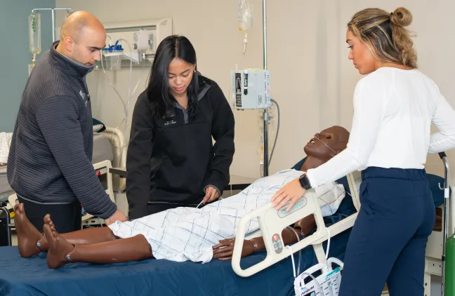 A group of health students practice diagnosing on a patient simulator in the Simulation Lab