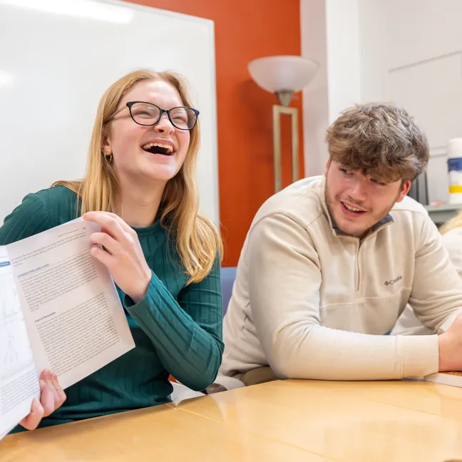 Two students smile as they review a textbook during class