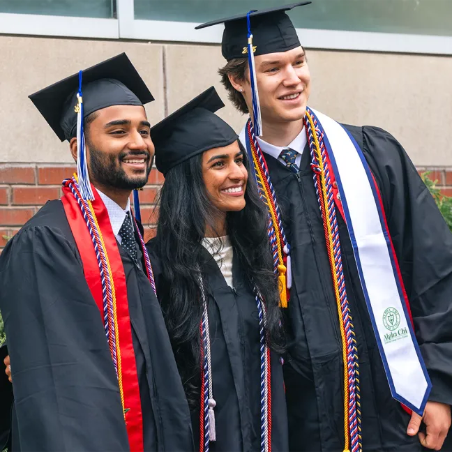 Three smiling students in graduation cap and gown pose together