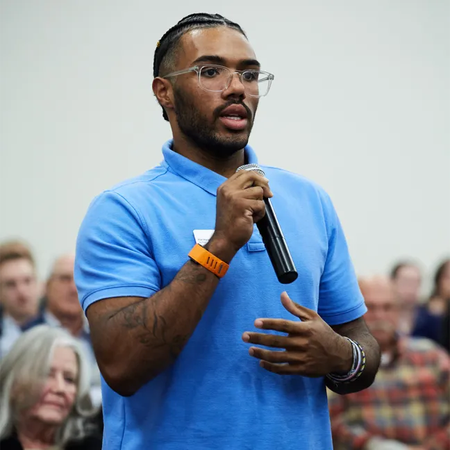 A student speaks into a microphone from a large audience