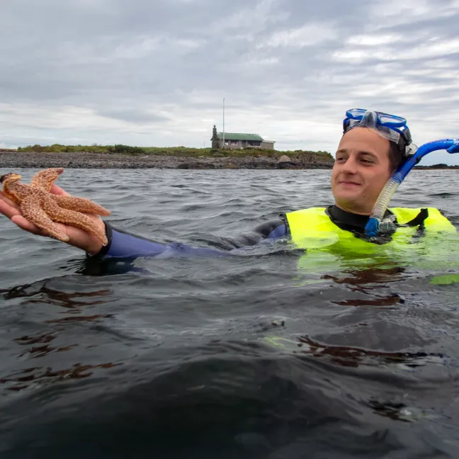 A student wearing snorkel gear holds up a starfish while in the ocean