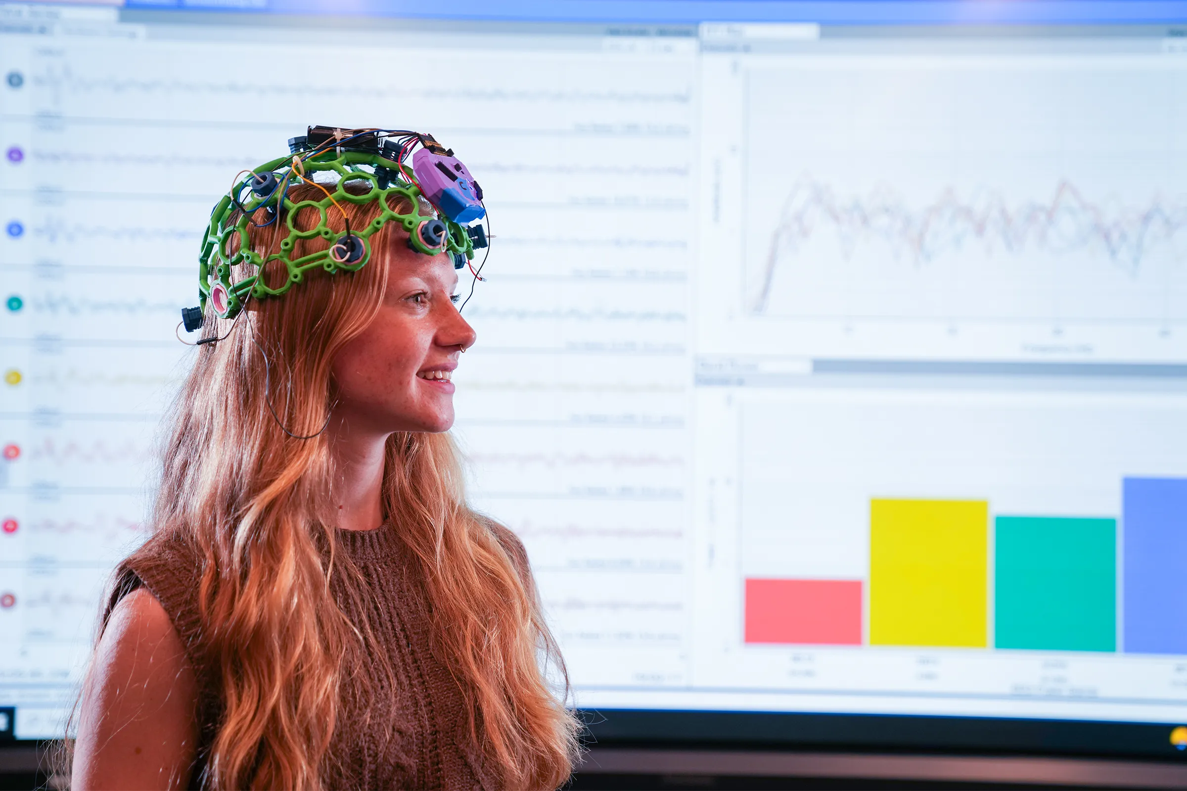 Jessica Howard stands in front of EEG brainwave data and colorful graphs displayed on large monitor.