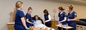 four students and a professor work on a patient simulator
