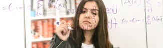 A female student works on math formulas on a dry erase board