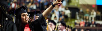 A woman in a cap and gown points to friends at UNE's 187th Commencement ceremony