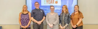 Five UNE alumni — Dawn McLaughlin, Joshua Chard, Lacey Todd, Katie Flannery, and Emily Rosser — are pictured against a whiteboard
