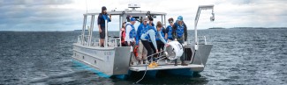 A group of students on a U N E boat retreive a white shark buoy from the ocean