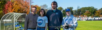 A faculty member and three students pose with a flying drone