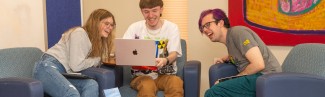 Three University of New England students sit together around a laptop