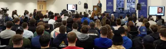A crowd of students listen to a speaker at a podium