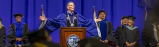 U N E President Herbert in regalia speaks at a podium to a crowd of students