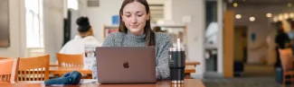 A student sitting at a table types on their laptop in a library