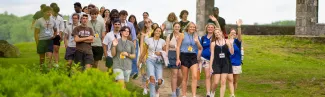 A large group of new U N E students walk and wave along a path at Jordan Point, with lanyards and name tags visible on their first day of orientation.