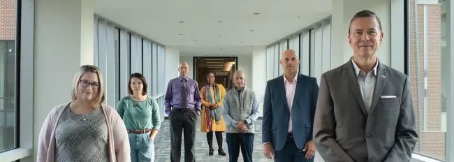 U N E faculty, a student, and President Herbert stand in a hallway