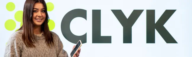 Abbie Anderson poses with a mobile phone. The name of her app, Clyk, is shown behind her
