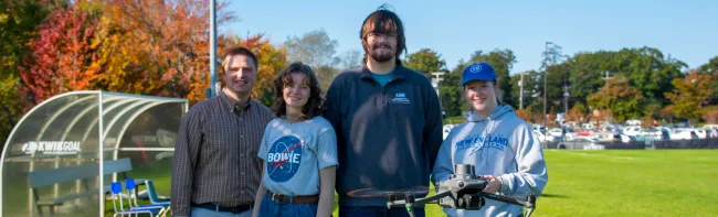 A faculty member and three students pose with a flying drone