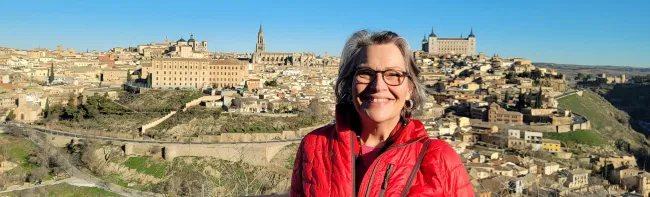 A woman smles for a photo in front of a countryside Spanish city 