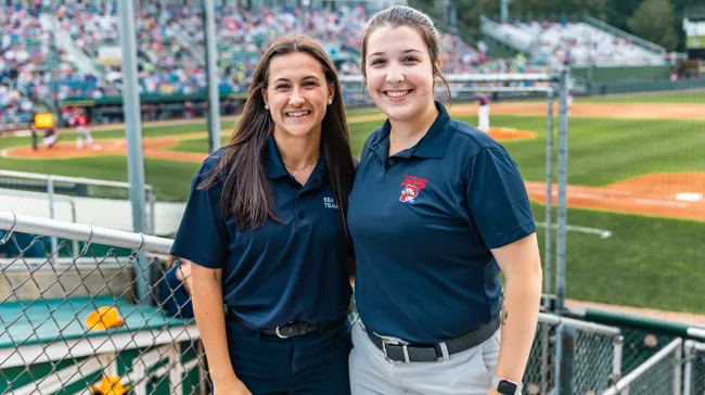 Two UNE business students pose in front of the baseball diamond at Portland's Hadlock Field
