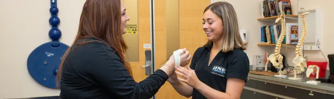A U N E Athletic Training student practices a wrist assessment technique on a classmate in a clinical training room.
