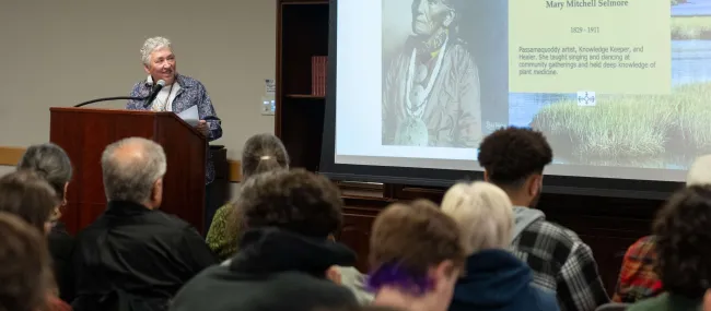 Poet Mikhu Paul speaks at a podium in UNE's St. Francis Room