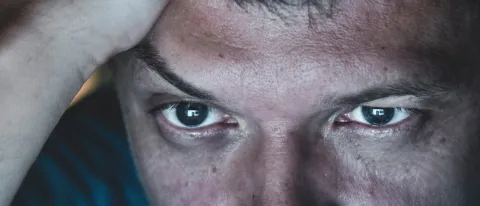 Image of man's eyes illuminated by computer screen, with pained expression.